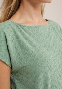 Vihreä teksturoitu pusero, jossa on herringbone-kuvio, veneen pääntie ja lyhyet hihat. Kankaan ilme on pehmeä ja kevyt.