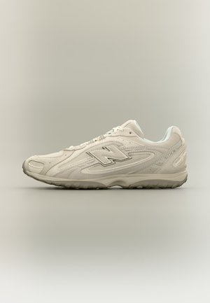 Hvit New Balance atletisk sneaker med "N"-logo, snøring og teksturert såle vist fra siden på nøytral bakgrunn.