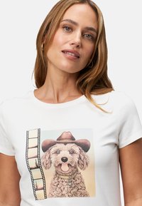 T-shirt en coton blanc avec un imprimé graphique d'un chien portant un chapeau de cow-boy, orné d'un collier et d'accents de bande film sur le côté.