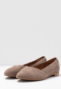Ballerines en matériau beige perforé, avec un design à bout pointu et un petit talon arrondi. Présentent une subtile accent sur le côté.
