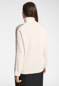 Jasnobeżowy golf z fakturowanymi szarymi detalami na ramionach, z długimi rękawami i luźnym krojem.