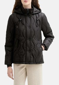 Veste matelassée noire avec capuche, dotée d'une fermeture éclair frontale, de boutons-pression et de cordons élastiques au col et aux poignets. Texture douce.