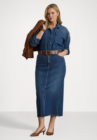 Denimskjorte, brun skinnjakke over skulderen, høyt liv denimskjørt med frontsplitt, brun belte og brune kittenheels.