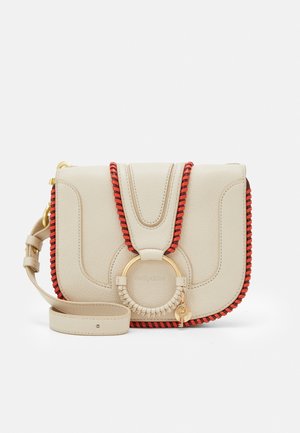 Petit sac bandoulière en cuir beige avec bordure rouge et noire, détail anneau doré et bandoulière réglable sur fond blanc.
