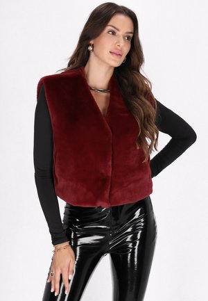 Bordeaux nepbont gilet met een kraaglijn, iets cropped ontwerp, gecombineerd met zwarte glanzende high-waisted broeken.