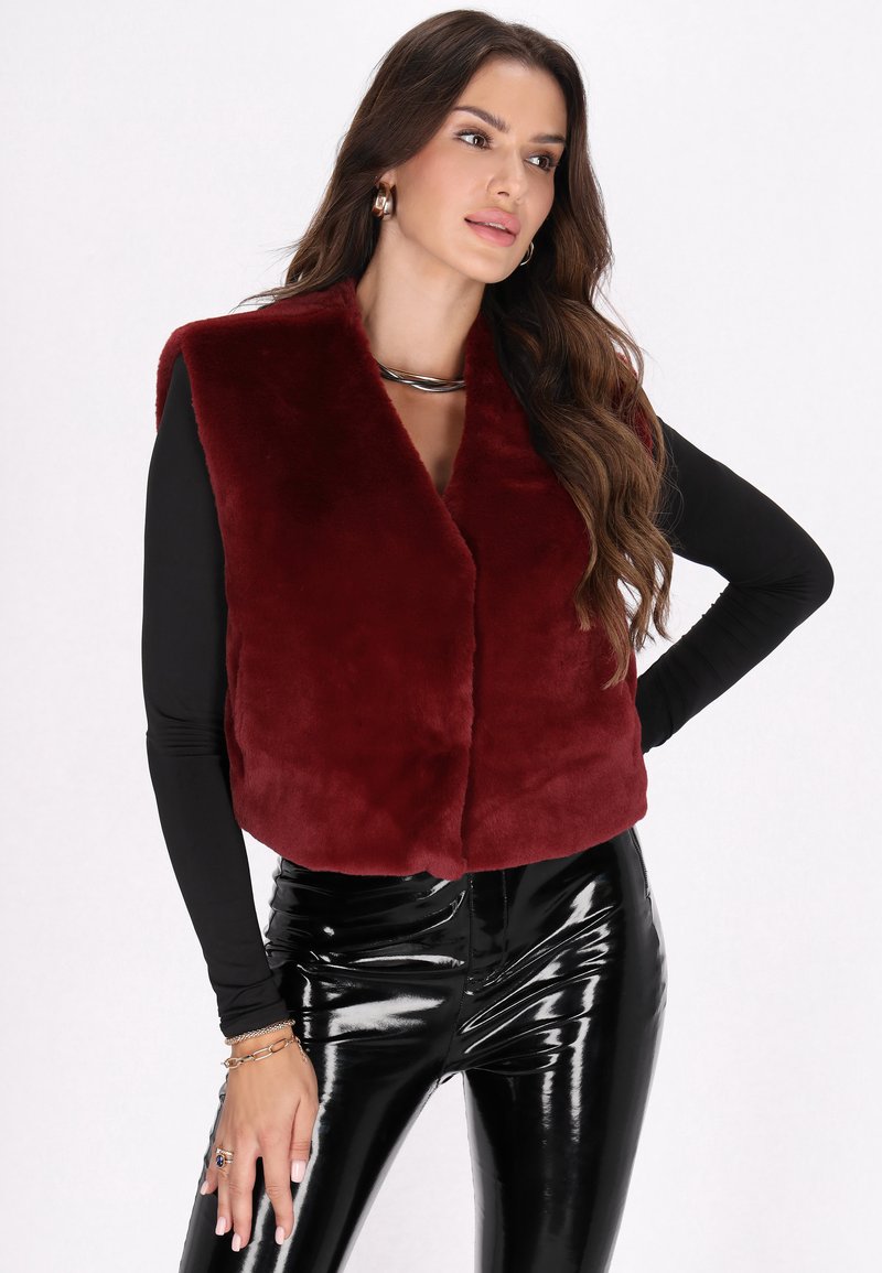 Bordeaux nepbont gilet met een kraaglijn, iets cropped ontwerp, gecombineerd met zwarte glanzende high-waisted broeken.