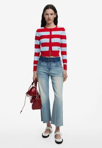 Röd och ljusblå randig cardigan, kroppsnära passform, kombinerad med ljusblå utsvängda jeans. Svarta och vita slip-on skor och en röd handväska.