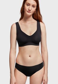 Soutien-gorge noir sans fil avec larges bretelles et décolleté en V, associé à une culotte de type bikini avec bords festonnés.