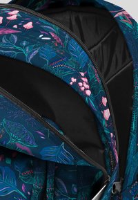 Reppu värikkäällä designilla, johon kuuluu laivaston sinisestä kankaasta valmistettu trooppinen lehti- ja kukkakuosi, musta sisävuori ja vetoketjullinen avaus.