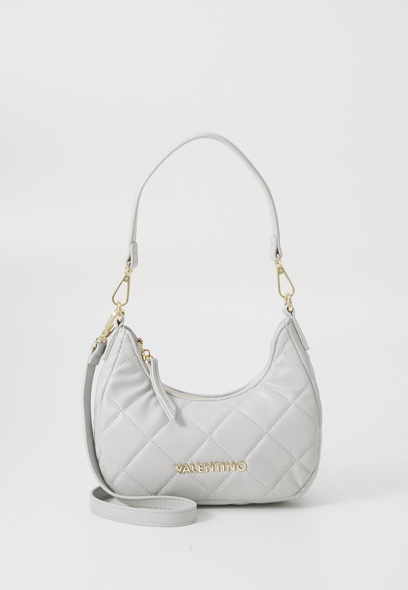 Bolsa de mão em pele cinza acolchoada com ferragens em dourado, uma alça curta e uma correia ajustável. Apresenta um formato arredondado e um discreto detalhe de logótipo.