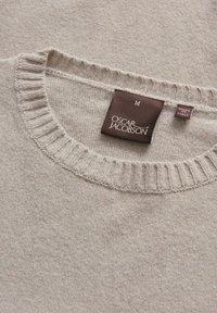 Pull en maille beige avec un col rond côtelé, arborant une étiquette brune indiquant "OSCAR JACOBSON" et "FABRIQUÉ EN ITALIE". Taille M.
