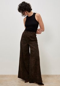 Leopardenmuster weit geschnittene Hose aus dunkelbraunem und schwarzem Stoff, kombiniert mit einem figurbetonten schwarzen Tanktop aus glattem Material und hoher Taille.