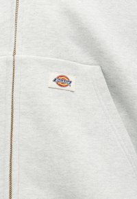 Ανοιχτό γκρι φούτερ με φερμουάρ και μικρό λογότυπο Dickies πάνω από την μπροστινή τσέπη στην αριστερή πλευρά.