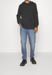 Svart hoodie med dragsko, texturerat tyg; kombinerad med ljusblå denimjeans och svarta snörkängor med tjock sula.