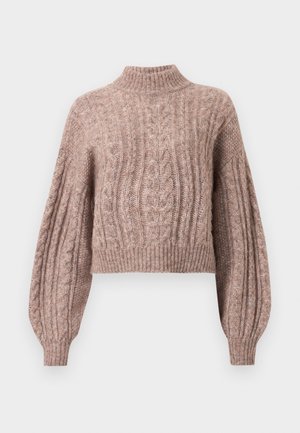 Sweter o kroju cropped z włóczki w delikatnym różowym odcieniu, z wysokim dekoltem oraz obszernymi rękawami zakończonymi ściągaczami. 