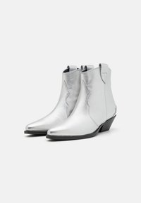 Botines de cuero plateado hasta el tobillo con puntera afilada, diseño ondulado y un tacón bajo y grueso. Textura suave y detalles de herrajes mínimos.