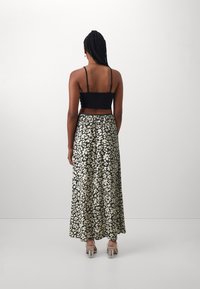 Černý crop top a dlouhá sukně s květinovým vzorem v krémové a černé barvě, se stahovaným pasem a transparentními blokovými podpatky.