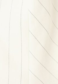 Tissu blanc avec des lignes pointillées noires subtiles formant des motifs courbes et diagonaux, mettant en valeur la texture et les détails des coutures.