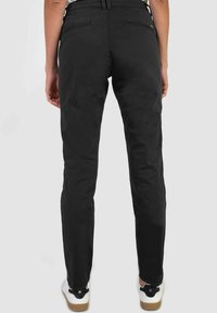 Zwarte katoenen chino's met een recht model, met achterzakken en een lichte glans. Gemonteerd met witte sneakers op een gestructureerd oppervlak.