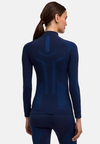 Maglia sportiva a maniche lunghe color blu navy con design aderente e dettagli strutturati. Presenta motivi contrastanti di blu più chiaro sulla schiena e sulle maniche.
