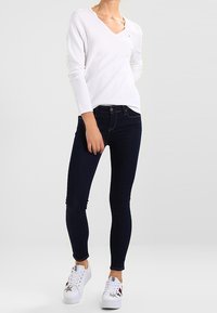 Valkoinen pitkähihainen V-kaula-aukollinen paita, yhdistetty tummansinisiin skinny-farkkuihin ja valkoisiin lenkkareihin, joissa on tähtikoristeita. Rentoon asuun sopiva yksinkertainen malli.