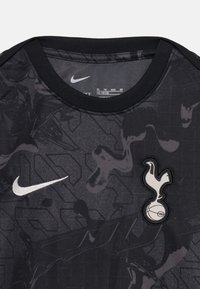 Svart Nike t-skjorte med teksturert design, grå abstrakte mønstre og en hvit Tottenham Hotspur-logo på forsiden.