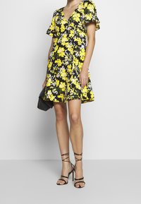 Vestido negro con estampado floral en amarillo, de mangas cortas y escote en V. Combinado con sandalias de tacón alto negras con tiras.