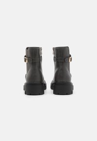 Botas de tobillo de cuero negro con una textura suave, con un detalle de hebilla dorada y una suela de goma resistente. Cierre de cremallera en la parte trasera.