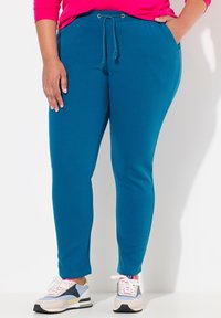 Turfärgad joggers gjorda av mjukt tyg, med en dragsko i midjan med metalldetaljer, tapered ben och sidofickor, tillsammans med flerfärgade sneakers.