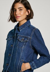Giubbotto in denim blu scuro con chiusura a bottoni, due tasche sul petto e un colletto classico con cuciture a contrasto e una vestibilità rilassata.