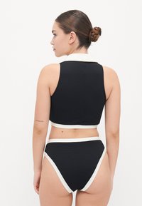 Black two-piece swimwear set with a textured finish, featuring a cropped top and high-waisted bikini bottoms accented by white trim.
