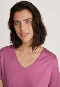 Korte roze V-hals t-shirt met korte mouwen. Gladde stof, casual pasvorm. Achtergrond is neutraal en onopvallend.