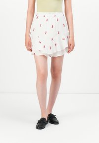 Falda blanca en capas con bordado floral rojo, cinturilla elástica y tela ligera. Combinada con zapatos negros para crear contraste.