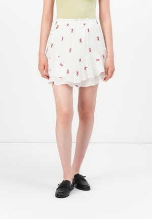 Fustă albă în straturi cu broderie florală roșie, talie elastică și țesătură ușoară. Combinate cu pantofi negri pentru contrast.