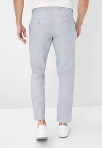 Light blue linen trousers with a tapered fit, featuring two back pockets and button closures, paired with white sneakers.