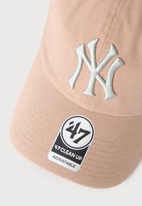 Ροζ καπέλο μπέιζμπολ με ασημί κεντημένο λογότυπο NY, ρυθμιζόμενο πίσω μέρος και μαύρη και λευκή ετικέτα που γράφει '47 CLEAN UP'. Υφασμάτινη υφή.