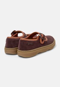 Zapatos de ante morado con una correa de cuero naranja y un detalle en forma de lazo, que cuentan con una suela acolchada y un sutil logotipo en la parte trasera.