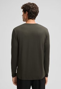 Langsleeve shirt in donker groen, gemaakt van een zachte, gestructureerde stof. Kenmerken zijn een ronde hals en een afgeronde zoom. Eenvoudig, minimalistisch ontwerp.