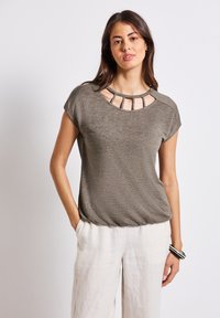Krátký rukáv olivově zelený top s kulatým výstřihem a detaily v oblasti výstřihu, volnější střih, v kombinaci s světlými lněnými kalhotami.