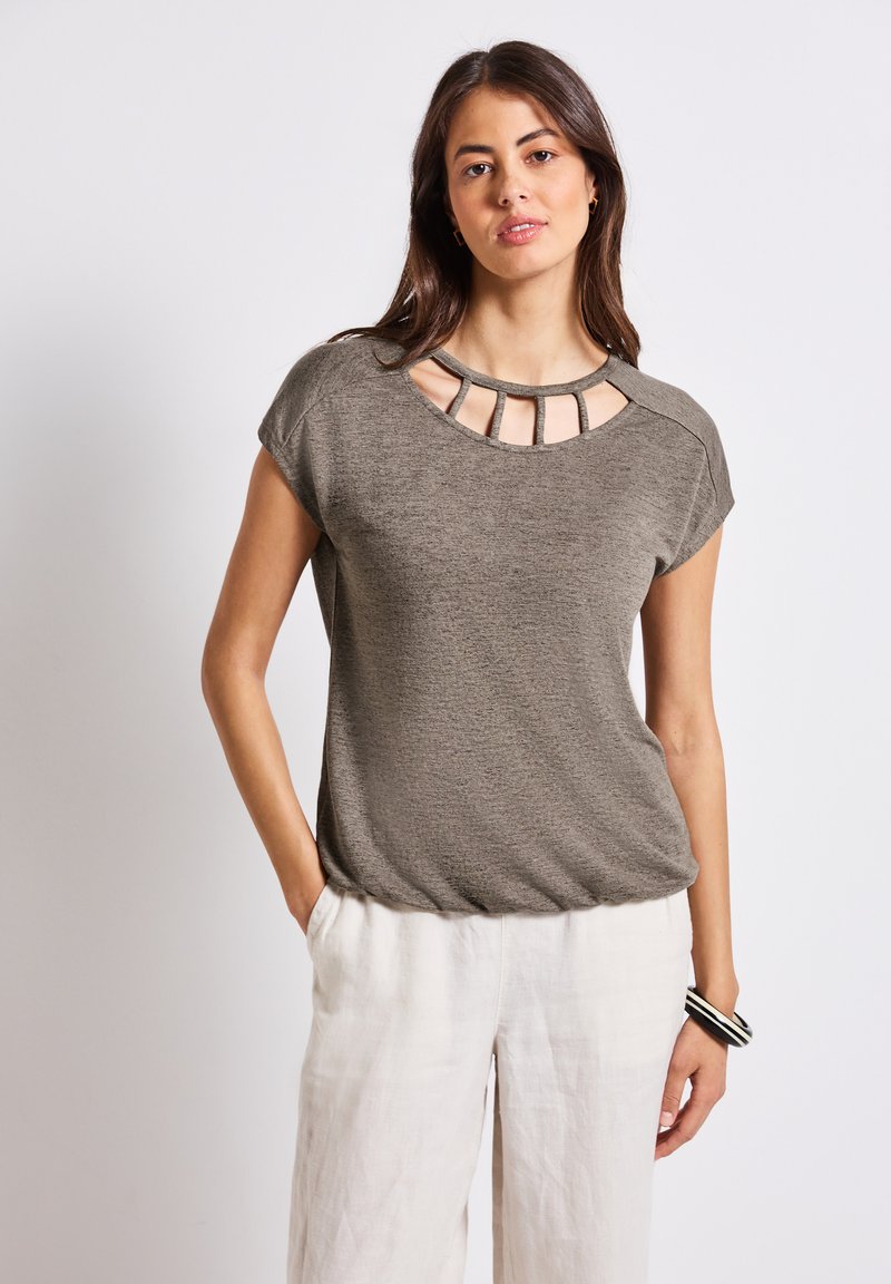 Krátký rukáv olivově zelený top s kulatým výstřihem a detaily v oblasti výstřihu, volnější střih, v kombinaci s světlými lněnými kalhotami.