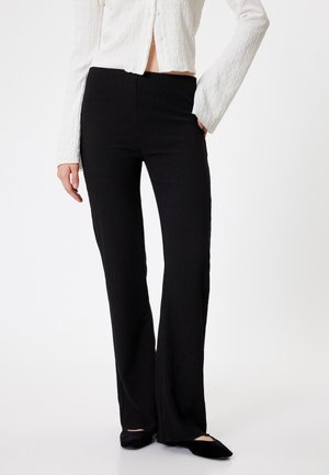 Pantaloni neri a zampa d'elefante con texture a costine e vita alta, abbinati a un top bianco a maniche lunghe con texture e ballerine nere.