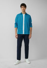 Lichtblauw linnen overhemd met knoopsluiting, gedragen over een wit T-shirt; gecombineerd met donkerblauwe broek en witte sneakers.