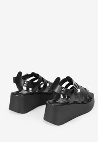 Sandalias de cuña negras con múltiples correas cruzadas, un detalle de hebilla, suela texturizada y un diseño de plataforma gruesa.