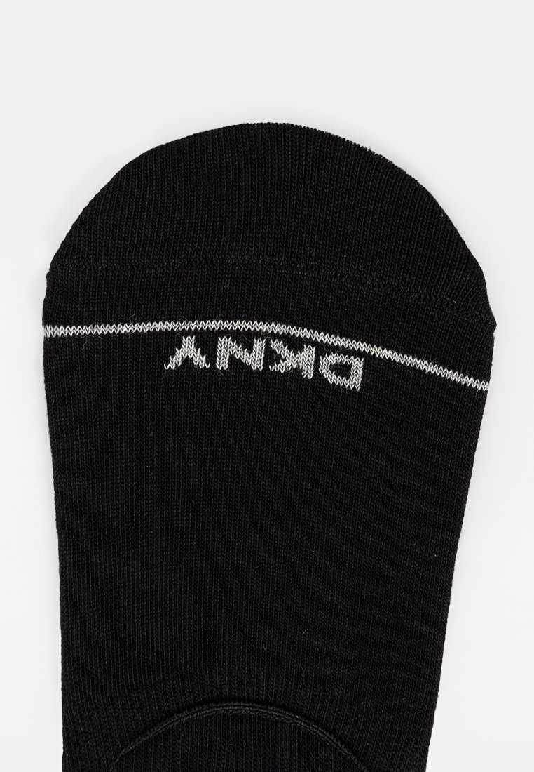 Zwarte enkelkous met een soepele breistekstuur, met witte tekst langs de bovenrand. Het ontwerp is minimalistisch en nauwsluitend.