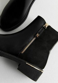 Zwarte enkellaarsjes van een combinatie van glad leer en suede, met een zijrits met gouden hardware en een lage blokhak.
