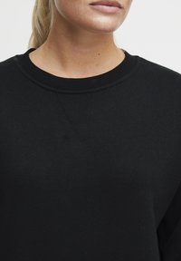 Svart sweatshirt med rund hals, ribbad krage och strukturerad tyg. Designen har minimal sömnad och en klassisk passform.