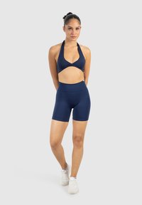 Marinblå halterneck sportbh med korsad framsidesdesign, kombinerad med högmidjade shorts. Tyget är mjukt och elastiskt, vilket gör det lämpligt för sportkläder.