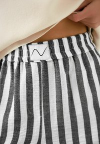Pantaloni scurți din in cu dungi alternative alb-negru, cu o talie elastică și o etichetă cusută cu un design minimalist.