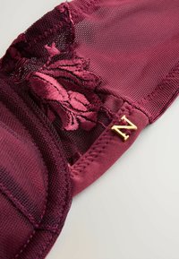 Bordeaux blondebh med blomsterbroderi, mesh-detaljer, polstrede skåle og en gylden 'N' accent. Glat stof med teksturerede elementer.