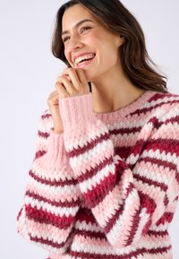Maglione lavorato a maglia con strisce orizzontali in tonalità di rosa, rosso e bianco. Polsini a costine spessi e texture morbida. Collo rotondo.
